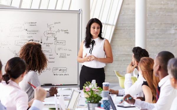 Businesswoman leading a meeting at a boardroom table in a bright room.