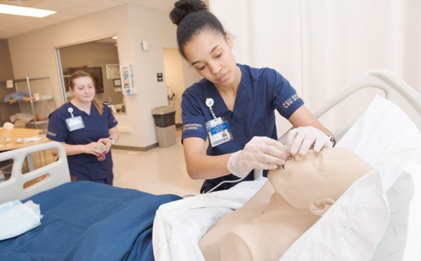 A nursing student inserting an air tube into a mannequin patient