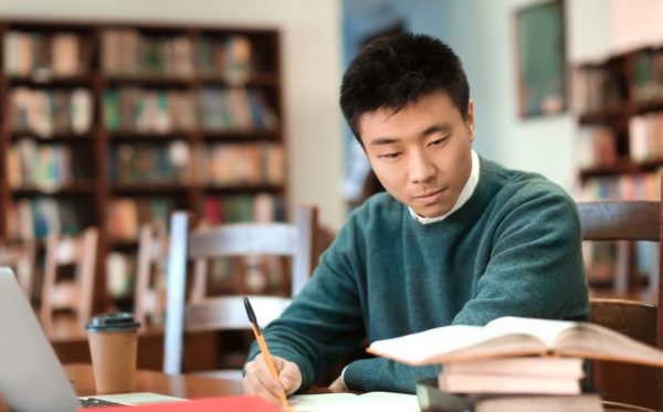 Asian student with laptop studying in library